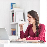 Woman biting pencil while working on computer