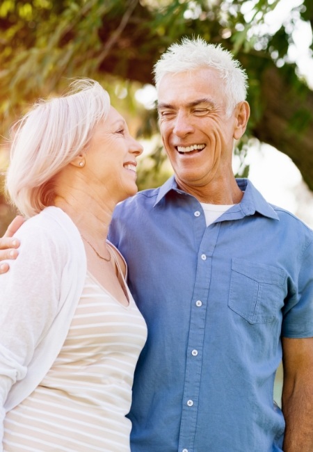 Man and woman with all on four dental implant dentures smiling outdoors