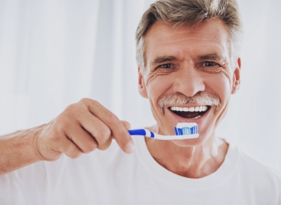 Man brushing teeth to care for all on four dental implants