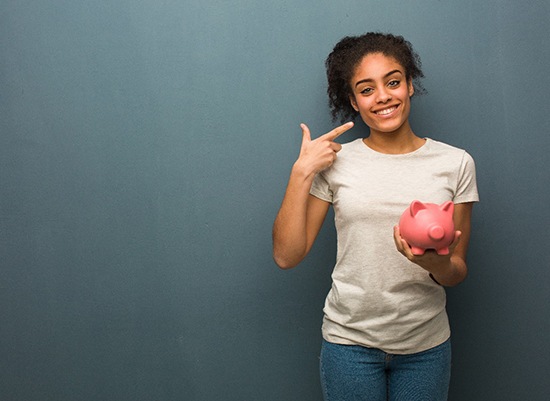 Someone holding a piggy bank and pointing at their teeth