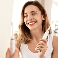 Woman with dental implants in Houston holding an electric toothbrush
