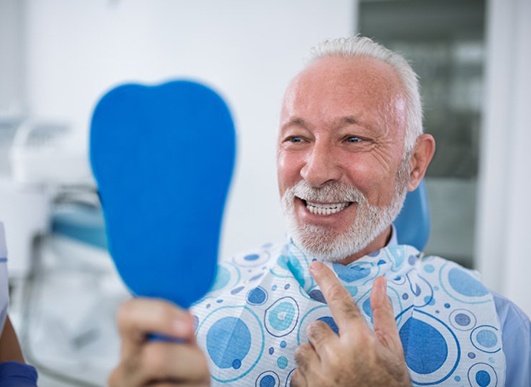 senior man pointing to his smile after dental implant salvage 