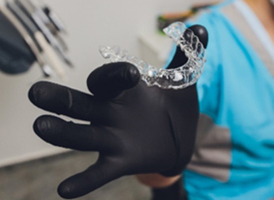 Dentist with black glove holding Invisalign aligner