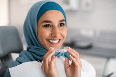 Smiling woman holding Invisalign aligners in dentist's office