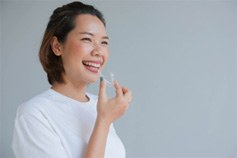 Smiling woman in white shirt holding Invisalign aligner
