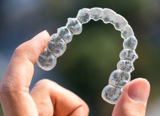 Hand holding up an Invisalign tray