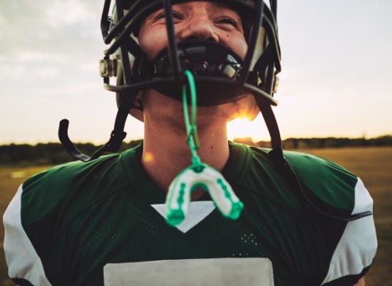 Teen boy with football helmet and green athletic mouthguard