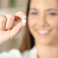 A blurred woman holding a pill between her fingers