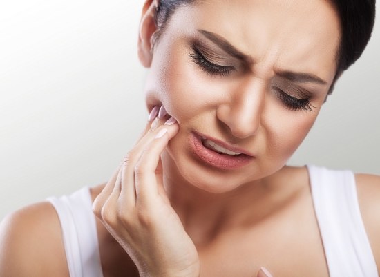Woman in need of endodontic treatment holding jaw in pain