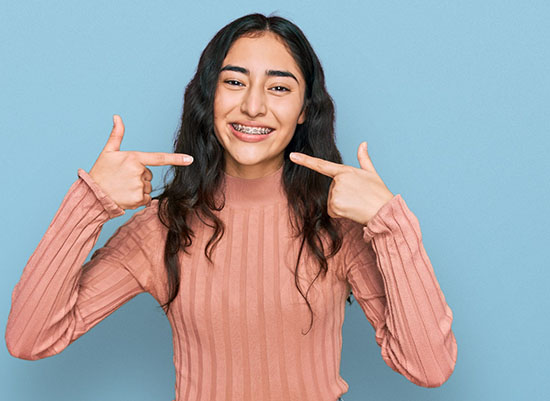 Young girl smiling while pointing to her braces