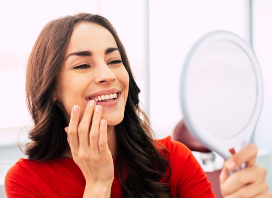 Woman looking at her smile after porcelain veneer treatment