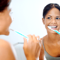 a woman brushing her teeth while looking in the mirror