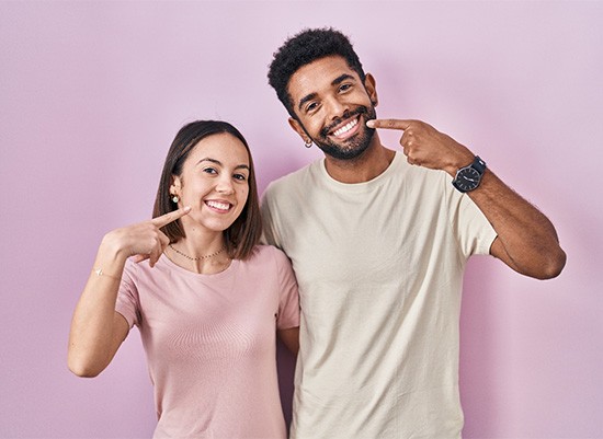 Young, happy couple pointing at their healthy teeth
