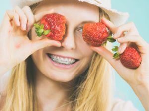Young woman with braces smiling and holding strawberries in front of her face