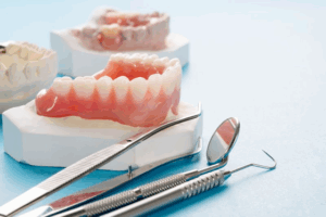 Dentures sitting next to dental tools on a blue surface